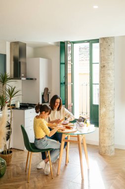 Anne ve kızı birlikte kurabiye hazırlıyorlar. Parlak, modern bir mutfakta, kaliteli zaman geçirmenin tadını çıkarıyorlar.