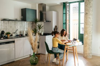 Anne ve kızı çikolatalı kurabiye yapıyor. Parlak mutfakta tablet üzerinde online tarifi takip ediyorlar.