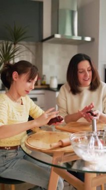 Anne ve kızı birlikte çikolatalı kurabiye yapıyorlar, modern mutfaklarında kaliteli zaman geçiriyorlar.
