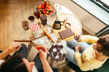 Anne ve kızı rahatlatıcı bir öğleden sonranın tadını çıkarıyor çikolatalı kurabiyeler hazırlıyor ve taze çilek yiyorlar.