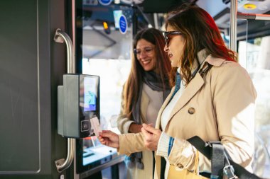 İki olgun bayan arkadaş alışveriş torbaları tutarken, alışveriş ve boş vakitlerin tadını çıkarırken, modern bir otobüse binmek için temas kurmadan para ödüyorlar.