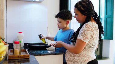 Hamile anne oğlunun kızartma tavasına yağ dökmesine yardım ediyor.