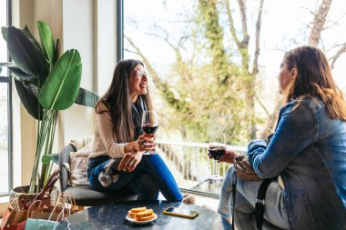 Alışveriş gezisinden sonra kafede kırmızı şarap içip sohbet eden iki kadın arkadaşlığı ve boş vakitleri kutluyorlar.