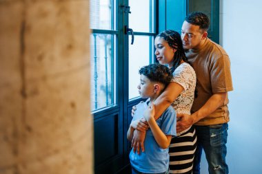 Latin hamile anne, baba ve oğul pencereden dışarı bakıyor.