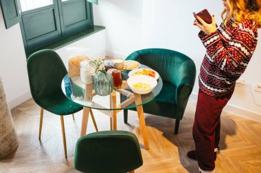 Pijamalı bir kadın sıcacık bir yemek odasında sağlıklı bir kahvaltı fotoğrafı çekiyor.