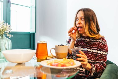 Evde kahvaltı yaparken yaban mersini yiyen mutlu bir kadın sağlıklı ve lezzetli bir yemeğin tadını çıkarıyor.