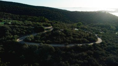 Sardunya tepelerinde kıvrılan, günbatımının sıcacık parıltısıyla yıkanan manzaralı bir yol manzarası.