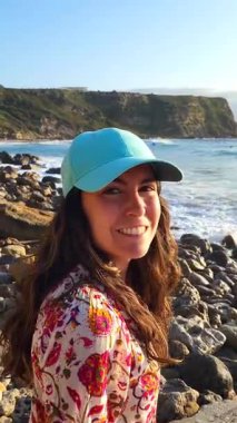 Şapka takan genç bir kadın yaz tatilinin tadını çıkarıyor takım elbiseli kayalık plajlarda, Cantabria, İspanya