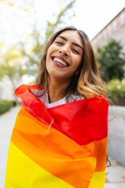 Lgbtqia 'yı kutlayan gökkuşağı bayrağına sarılı mutlu genç bir kadının portresi artı gurur ayı