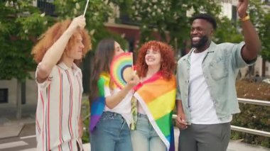 Gökkuşağı bayrakları sallayan ve dışarıda LGBT onur ayını kutlayan çok uluslu arkadaşlar.