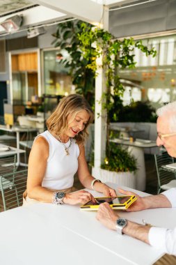 Üst düzey işadamları dijital tablet kullanıyor, restoranda sözleşme tartışıyorlar.
