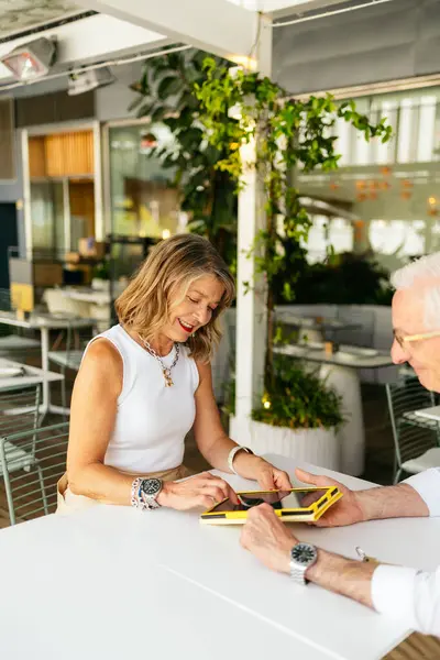 Üst düzey işadamları dijital tablet kullanıyor, restoranda sözleşme tartışıyorlar.