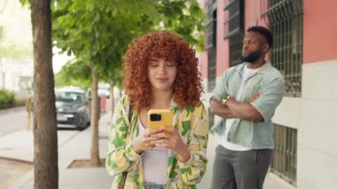 Genç kızıl saçlı kadın akıllı telefonunu kullanıyor ve bir erkeğin yanında gülümsüyor.