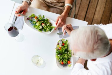 Bir restoranda taze salata yiyen yaşlı çift, yaşlılıkta sağlıklı yaşam tarzını ve sağlığını destekliyor.