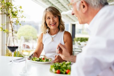 Mutlu emekli çift taze salata yiyor ve restoranda şarap içiyor. Sağlıklı yaşam tarzlarının tadını çıkarıyorlar.