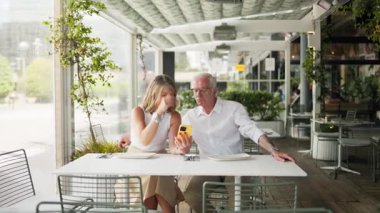 Akıllı telefonlara bakıp açık hava restoranında yemek yiyen mutlu çift.