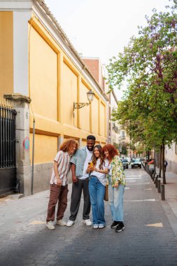 Şehir caddesinde akıllı telefon kullanan dört genç arkadaş birlikte vakit geçiriyorlar.