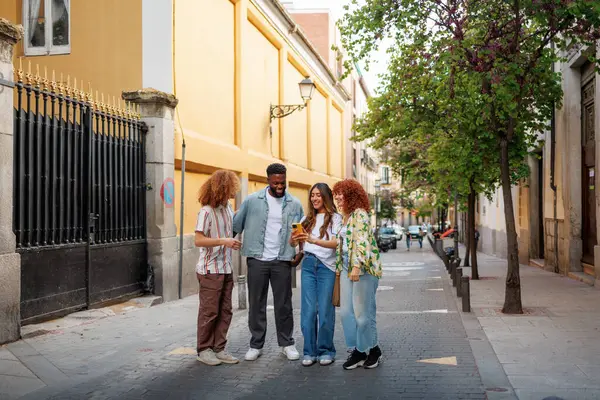 Dört genç ve etnik çeşitlilikte arkadaş akıllı telefon kullanıyor, şehirde eğleniyorlar..