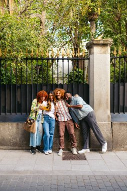 Dört neşeli çoklu etnik arkadaş akıllı telefonlarıyla selfie çekiyor ve şehirde birlikte vakit geçiriyorlar.
