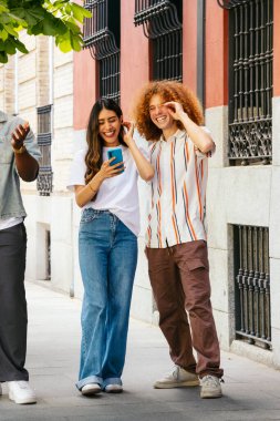 Çok ırklı bir arkadaş grubu açık havada yürürken akıllı telefondan müzik dinliyor.