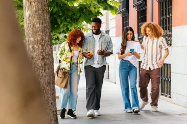 Bir grup genç öğrenci kaldırımda yürürken akıllı telefon kullanıyor.