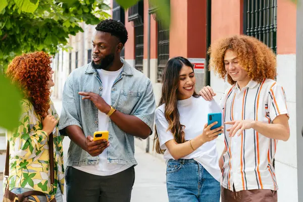 Dört çok ırklı arkadaş şehirde yürüyüş yapıyor, akıllı telefonlar kullanıyor ve sohbet ediyorlar.