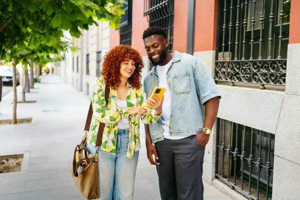 İki arkadaş sokakta yürüyorlar, akıllı telefona bakıyorlar ve gülümsüyorlar.