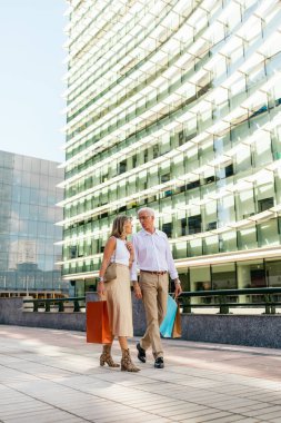 Alışveriş yaptıktan sonra şehirde yürüyen mutlu bir emekli çift.