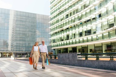 Yaşlı çift şehirde geziyor ve alışveriş torbaları taşıyor..