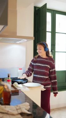 Modern mutfakta kahvaltı hazırlarken müzikten hoşlanan genç bir kadın.