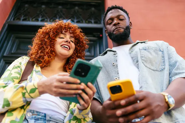 İki arkadaş akıllı telefonları kullanarak, içeriği paylaşarak ve dışarıda eğlenerek eğleniyorlar.