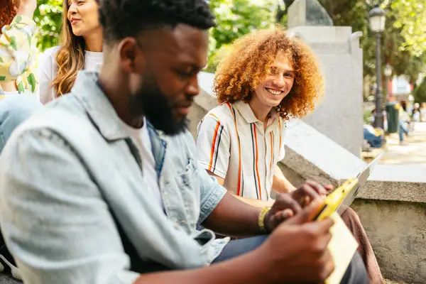 Öğrenciler parkta dizüstü bilgisayar kullanarak takım çalışmasını ve modern öğrenmeyi gösteren bir proje üzerinde birlikte çalışıyorlar.