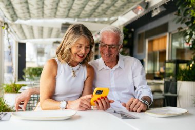 Restoran masasında otururken cep telefonu kullanan mutlu yaşlı çift.
