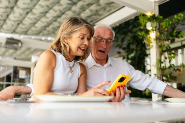 Restoranda yemek yerken cep telefonu kullanan mutlu yaşlı çift.