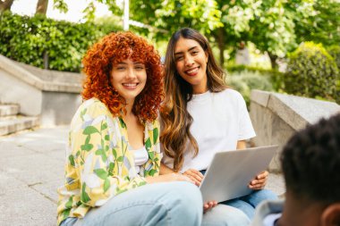 İki mutlu üniversite öğrencisi dizüstü bilgisayarda çalışıyor, kampüste güzel havanın tadını çıkarıyorlar.