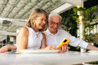 Restoranda akıllı telefon kullanan mutlu çift, birlikte vakit geçiriyorlar ve mobil teknolojiyi keşfediyorlar..