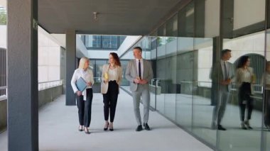 Modern ofis koridorunda yürüyen ve konuşan iş adamları