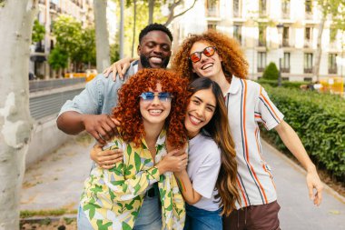 Bir grup neşeli arkadaş bir parkta kucaklaşıp gülümsüyor ve birlikte vakit geçiriyorlar.