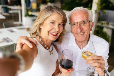 Restoranda şarap içerken selfie çeken yaşlı çift.