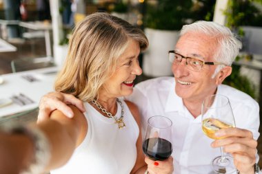 Restoranda şarap içerken selfie çeken yaşlı çift.