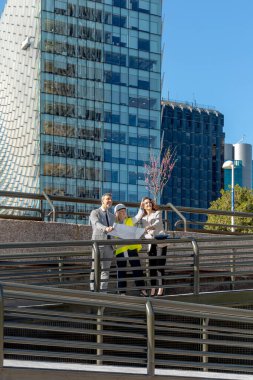 Mimarlar ve mühendisler modern binanın önündeki planı tartışıyorlar.