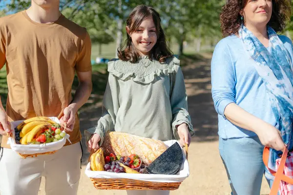 Güneşli bir günde parkta yürüyen piknik sepetleri taşıyan aile.