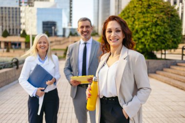 Kentsel alanda gülen iş adamları ellerinde belgeler ve yeniden kullanılabilir su şişesi tutuyorlar.