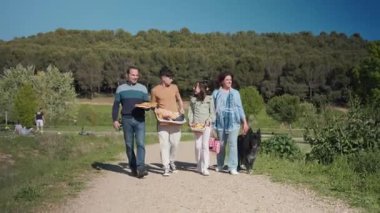 Mutlu aile parkta piknik sepetleri ve köpeklerle yürüyor.