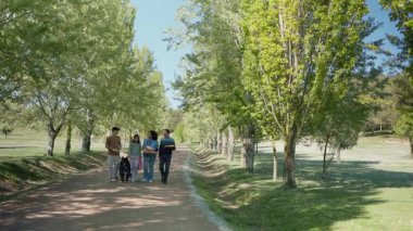 Aile ağaçlarla dolu bir yolda yürüyor piknik malzemelerini ve köpeklerini taşıyor.