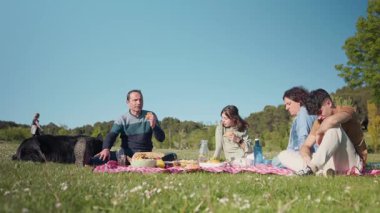 Aileleri güneşli bir parkta köpekleriyle piknik yapıyor.