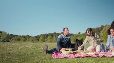 Parkta köpeğiyle güneşli pikniğin tadını çıkaran bir aile.