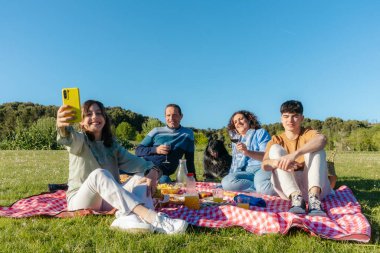Mutlu aile, köpekleriyle parkta piknik yaparken selfie çekiyor.