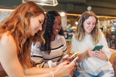 Friends smiling and using cell phones in bar