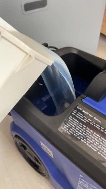 Profesyonel bir temizlik makinesinin su deposuna mavi temizlik çözeltisi döken beyaz bir konteynırın yakın çekim görüntüsü, sıvının akışını vurguluyor..